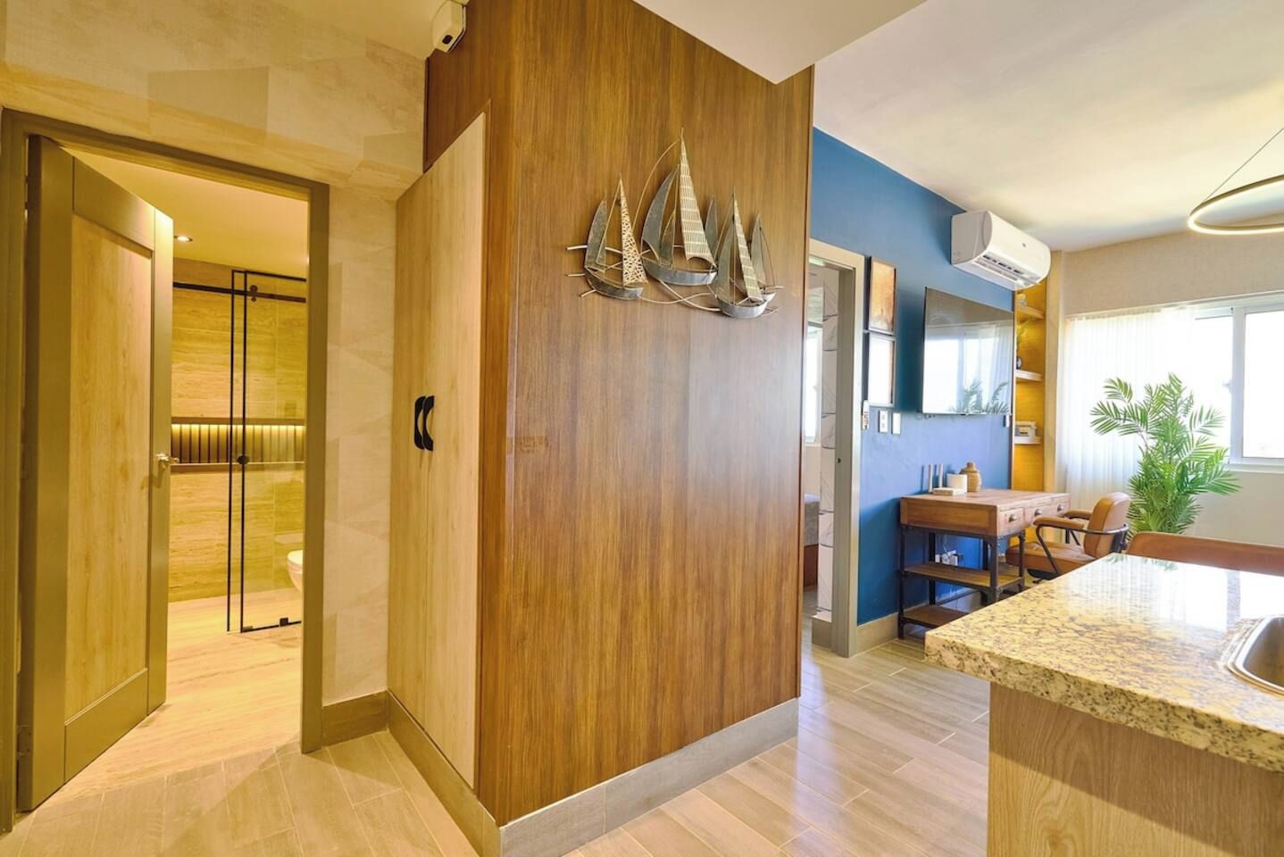 A modern interior with a wooden accent wall, a kitchen area with a dining table, and a visible bathroom with a glass shower enclosure.