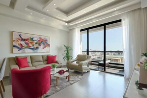 A modern living room with a sofa, armchair, and coffee table, a large abstract painting, and a city view through large windows. - ® {Art~City~View} @Downtown SDQ +Pool+Gym+KingBed (Santo Domingo)