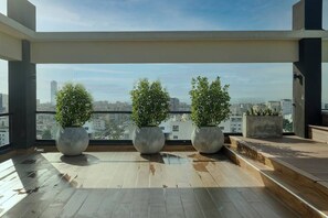 Une terrasse sur le toit, agrémentée de trois grands pots de plantes, d’une terrasse en bois et offrant une vue sur la ville.