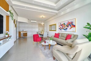 A modern living room with a sofa, red armchair, and a dining area in the background. -  ® {Art~City~View} @Downtown SDQ +Pool+Gym+KingBed (Santo Domingo)