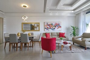Ein modernes Wohnzimmer mit Essbereich, einer Sofagarnitur, einem roten Sessel, einem Couchtisch und einem großen abstrakten Gemälde.
