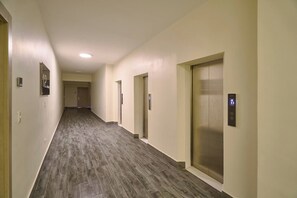 Ein Korridor mit Holzboden, beige gestrichenen Wänden und mehreren Türen, darunter ein Aufzug.