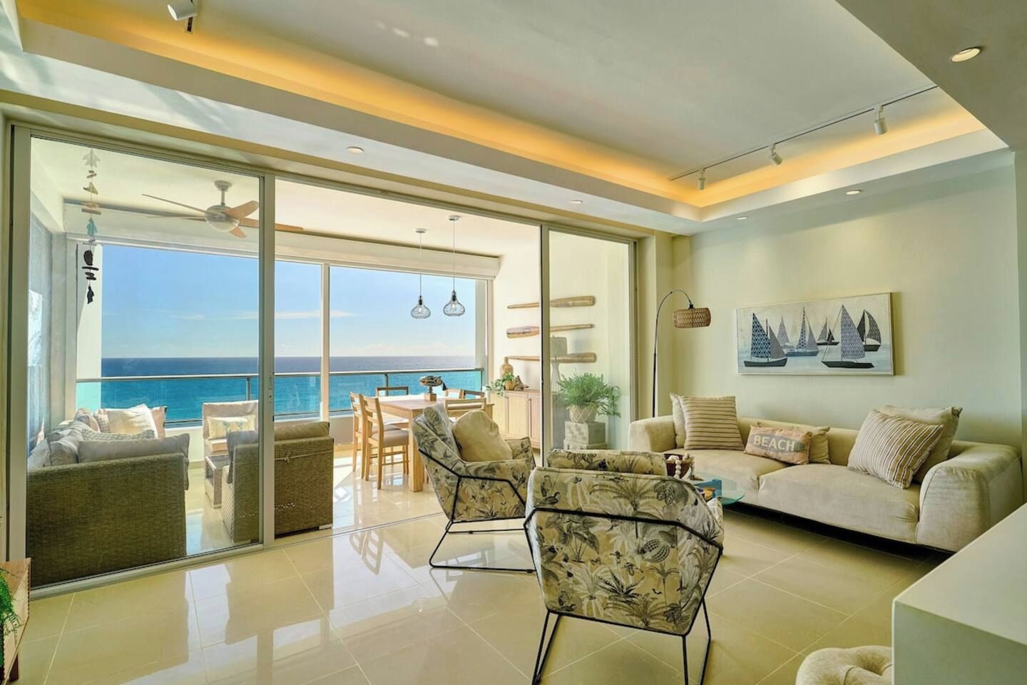 Amplia sala de estar con balcón con vistas al mar, amueblada con sofás y sillones, y un comedor con mesa y sillas.