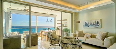 Amplia sala de estar con balcón con vistas al mar, amueblada con sofás y sillones, y un comedor con mesa y sillas.