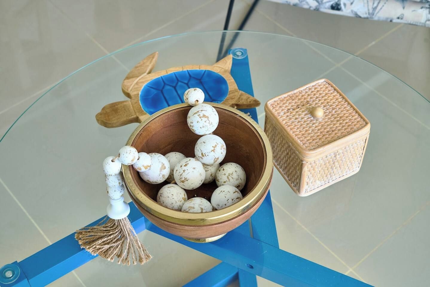 Una mesa de vidrio con un tazón de madera que contiene huevos, una cesta tejida y una silla azul.