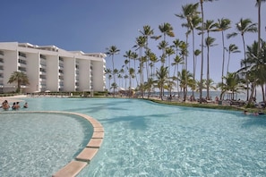 A resort pool with clear water, surrounded by palm trees and a hotel building. - ®{Marbella~LUX~Essence} Beachfront+Pool+11thFloor (Playa Juan Dolio)