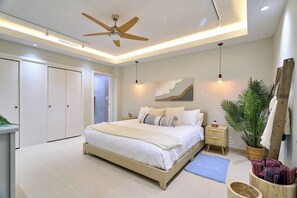 A bedroom with a bed, bedside tables, a ceiling fan, a wall-mounted artwork, a potted plant, and a wooden ladder leaning against the wall. - ®{Marbella~LUX~Essence} Beachfront+Pool+11thFloor (Playa Juan Dolio)