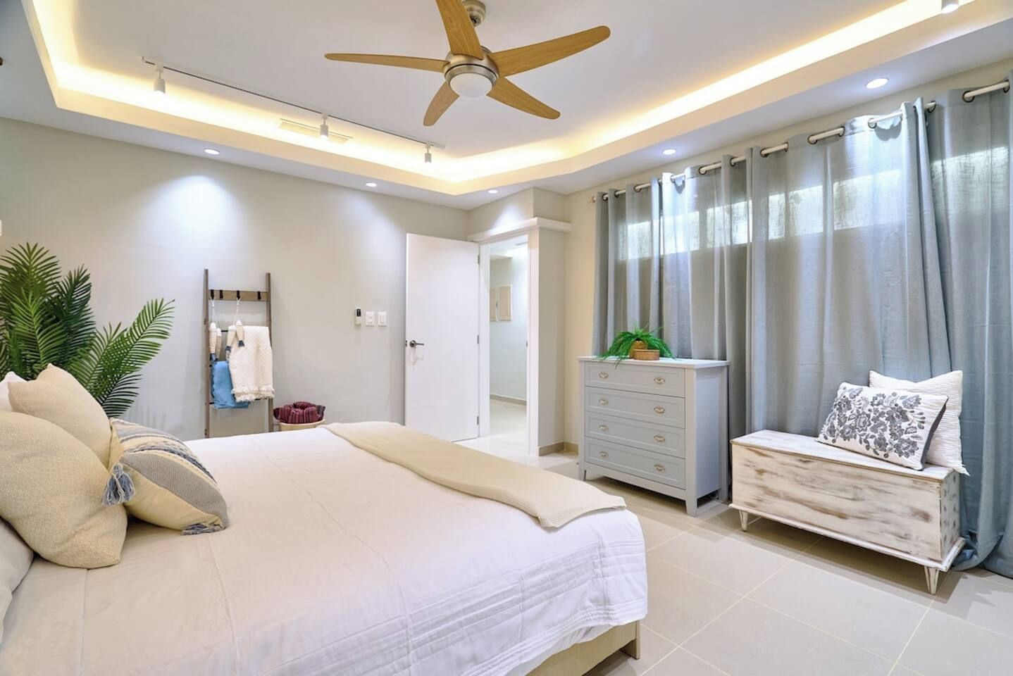 Une chambre à coucher moderne avec un lit, une commode, un ventilateur de plafond et une porte de salle de bain.