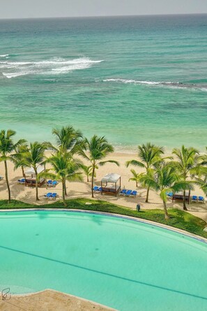 Ein Strandhotel mit Pool, Palmen und Liegestühlen.