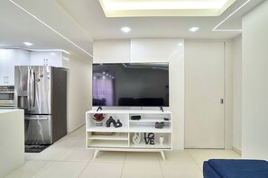 A modern kitchen with a built-in refrigerator, a flat-screen TV on a white stand, and a blue sofa in the living area. - ®{San~Angel~View} @DowntownSD +BBQ+Close-to-Mall (Santo Domingo)