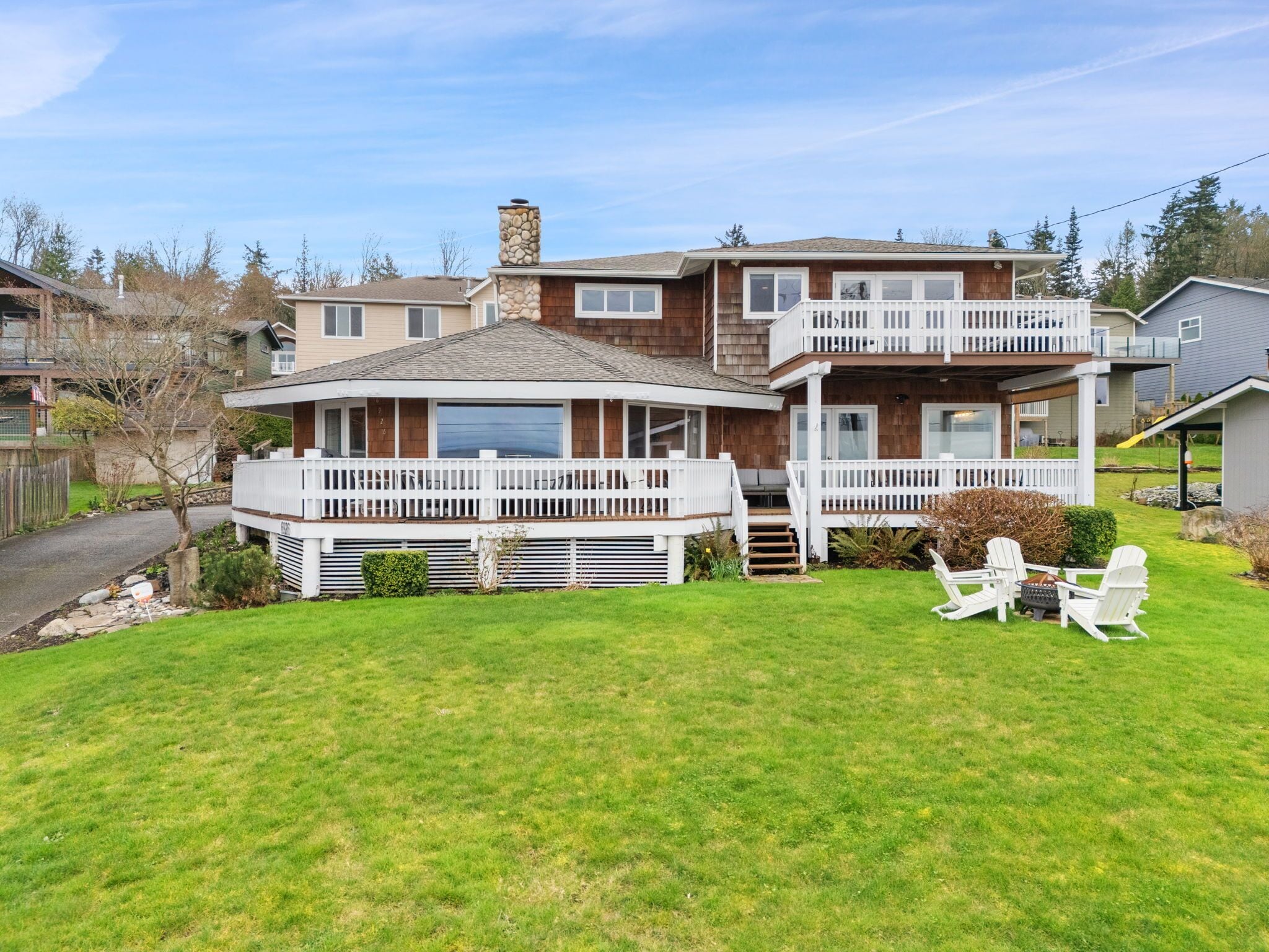 Charming two-story property featuring wraparound deck and spacious lawn in peaceful residential neighborhood.