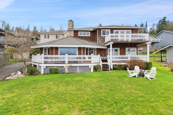 Charming two-story property featuring wraparound deck and spacious lawn in peaceful residential neighborhood.