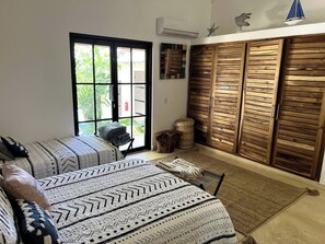 A room with a large window, a bed with patterned bedding, a wardrobe with horizontal slats, and a small table with a chair. - 4BR{Beach~by~Melo} @LosNomadas +2Min Beach+Pool (Las Terrenas)