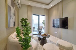 Un salon moderne avec un canapé, une table basse, un téléviseur fixé au mur et une vue sur l’extérieur grâce à une grande fenêtre.