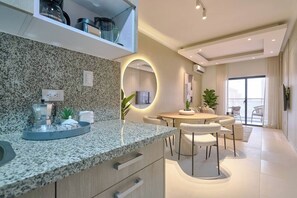 Een moderne keuken met granieten aanrecht, een koffieapparaat en een eethoek met een ronde tafel en stoelen.