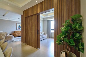 A modern living room with a sliding wooden door leading to another room, a large green plant, and a beige sofa. - 3BR Elegant Spot @DowntownSD +Family+Pool (Santo Domingo)