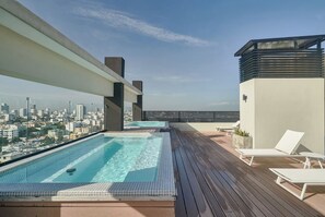 Una piscina sul tetto con vista sulla città, un pontile in legno e sedie a sdraio.