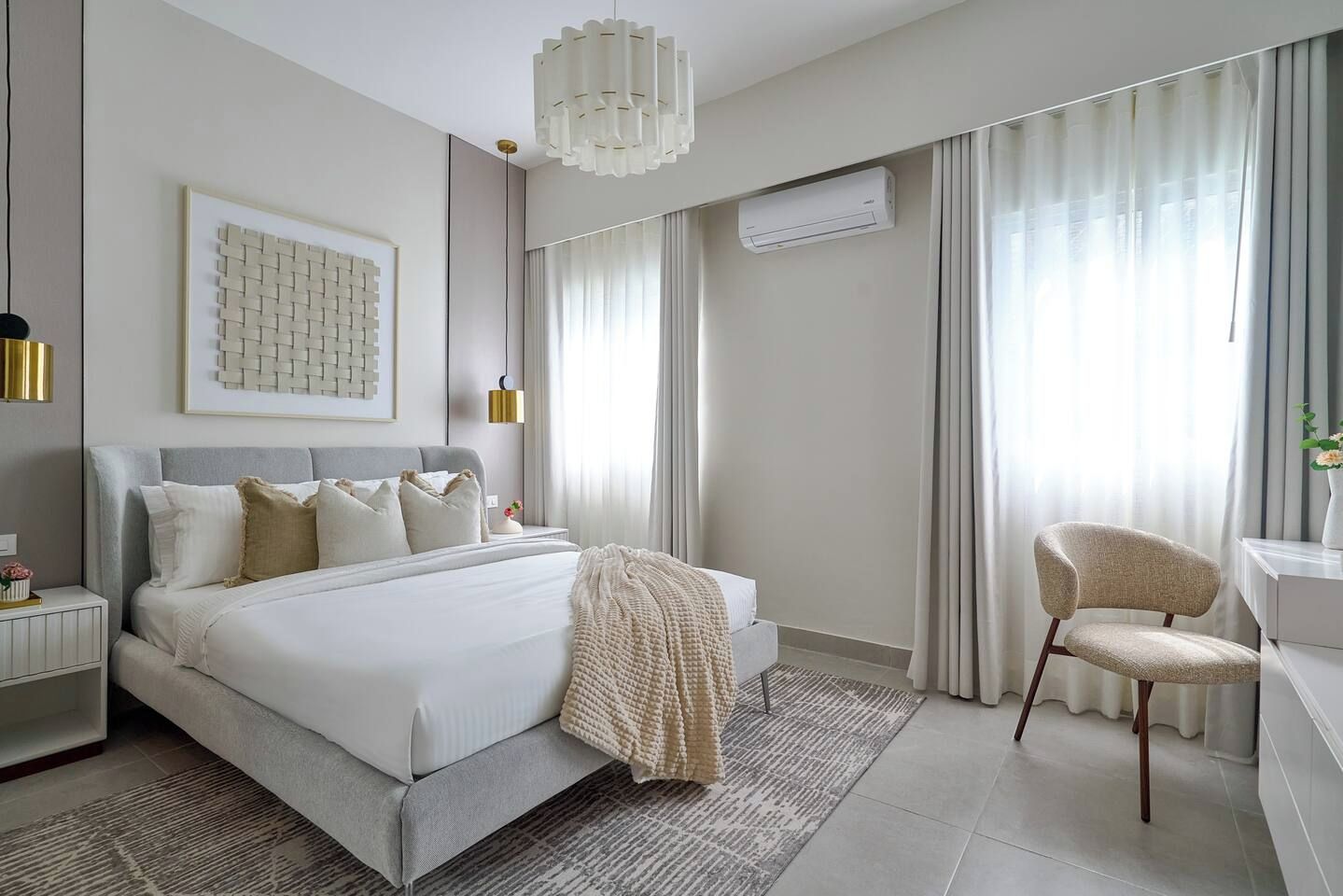A modern bedroom with a large bed, bedside tables, a chair, and a hanging light fixture.