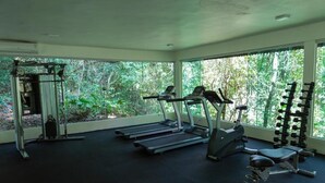 A gym with treadmills, a bench, and weight machines, with large windows overlooking greenery.