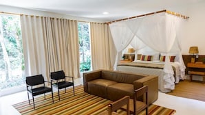 A bedroom with a canopy bed, a sofa, two chairs, and a large window with curtains.
