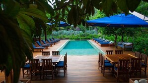 A poolside area with lounge chairs and tables, surrounded by greenery.