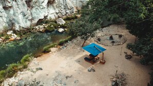 A campsite with a blue tent, a fire pit, and a clear stream.