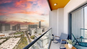 A balcony with a cityscape view, a chair, a small table, and a potted plant. - Cozy 1BR Retreat,  Prime Location (Dubai)