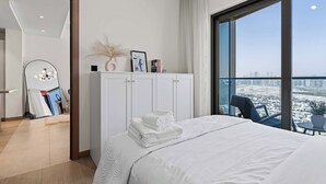 Habitación de hotel con cama, armario blanco, ventana grande con vista a la ciudad y balcón con una silla.