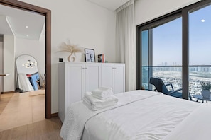 A hotel room with a bed, a white wardrobe, a large window with a city view, and a balcony with a chair. - Cozy 1BR Retreat,  Prime Location (Dubai)
