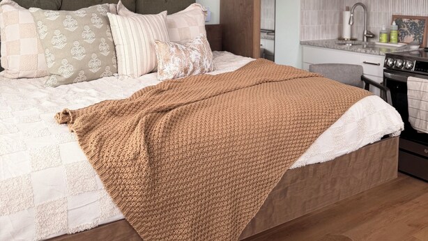 A modern bedroom with a bed, a wooden headboard, a ceiling fan, and a kitchen area with cabinets and appliances.