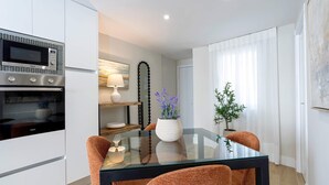 A modern kitchen with a built-in oven, a glass dining table with orange chairs, and a potted plant on the windowsill. - Genteel Home Almanzor (Cordoba)