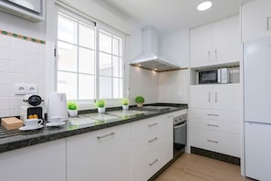 Een moderne keuken met witte kasten, een magnetron, een koffiezetapparaat en potplanten.