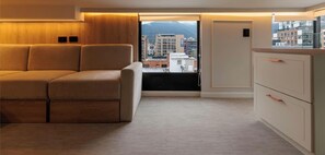 Eine moderne Wohnung mit Sofa, Küchenzeile und Blick auf Gebäude und Berge.
