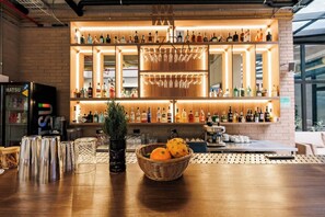 Una zona de bar con estantes llenos de botellas y vasos, un refrigerador y una mesa con un cesto de naranjas.