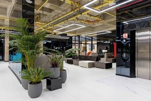 Eine moderne Lobby mit Sitzbereichen, Topfpflanzen und einem sichtbaren Aufzug.