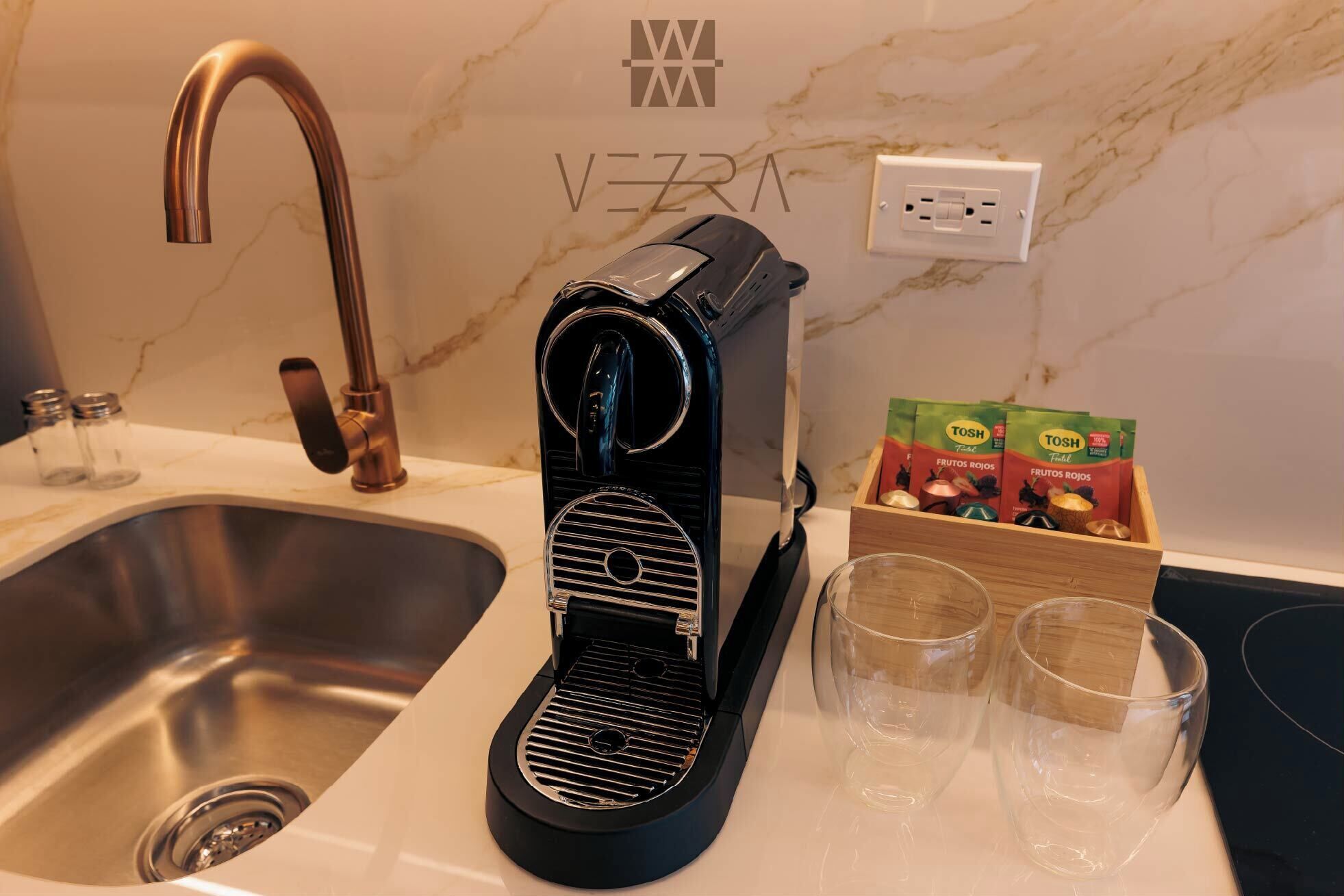 A kitchen with a modern espresso machine, a sink, and a box of TOSH fruit snacks.