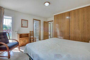 A bedroom with a bed, wooden wardrobe, a desk with a chair, and a mirror on the wall. - Villa Friesland – Pleasant Villa with Pool in a Peaceful Setting (Calonge)
