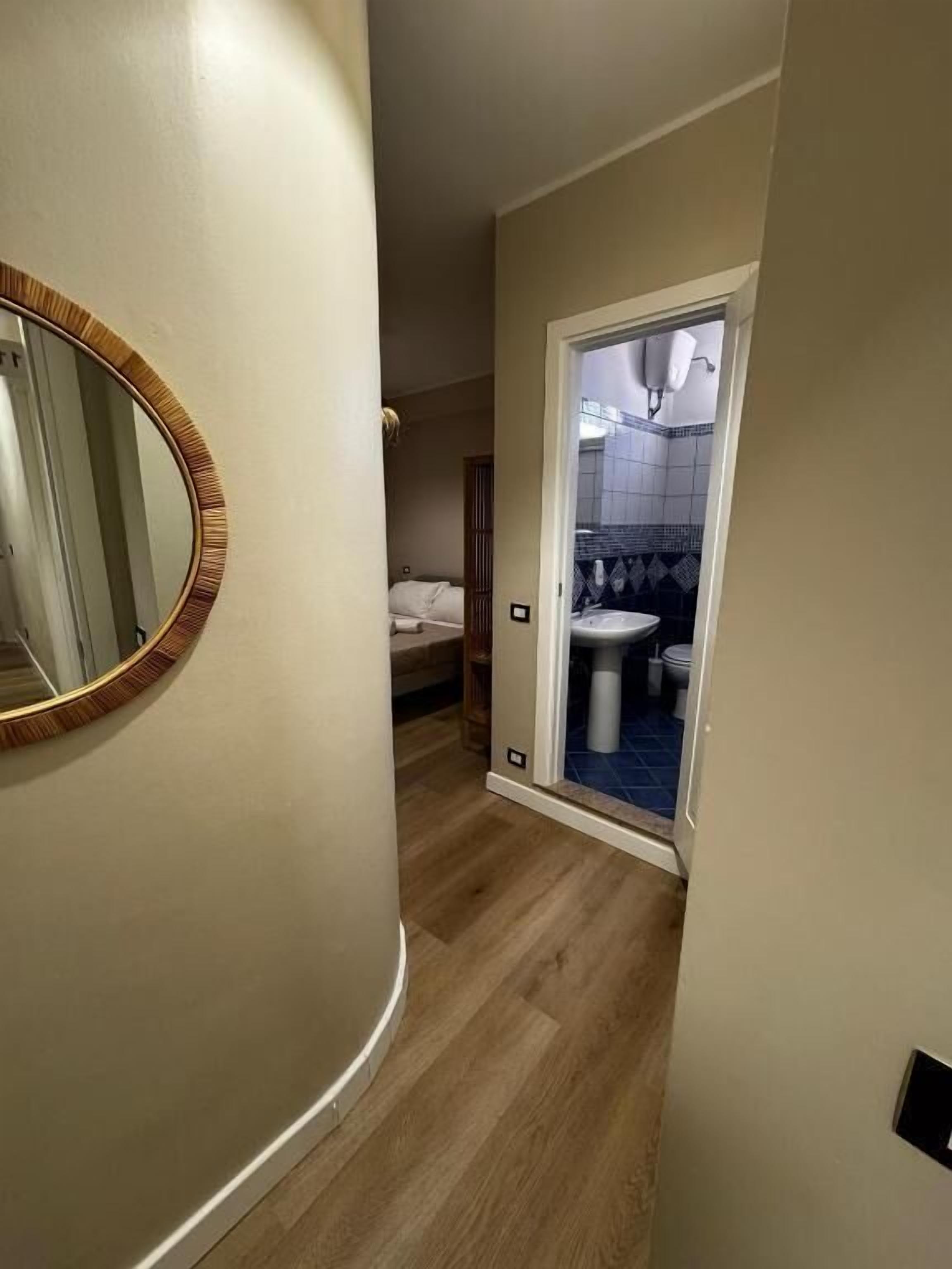 A hallway leading to a bathroom with a toilet, sink, and mirror.