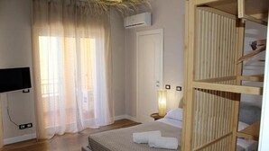 A bedroom with a bed, a TV, a wooden wardrobe, a window with curtains, and an air conditioning unit. - Paguro Beach Hotel  (Siculiana Marina)