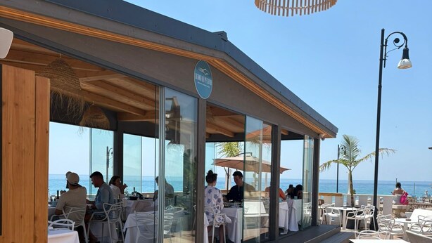 An outdoor dining area with tables and chairs, a wooden deck, and a view of the sea. - Paguro Beach Hotel  (Siculiana Marina)