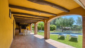 Ein überdachter Patio-Bereich mit Grillmöglichkeit, Sitzgelegenheiten im Freien und einem Swimmingpool.