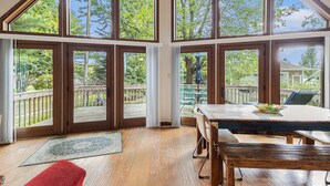 Quarto com janelas amplas, um deck de madeira e uma mesa de jantar com cadeiras.