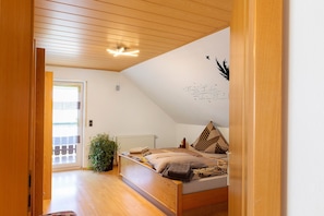 Et soveværelse med skrå vægge, en seng med mønstret sengetøj, en radiator og en potteplante.