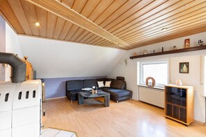 Et loftrum med skråvægge, en hjørnesofa, et sofabord, en radiator og et vindue med udsigt.
