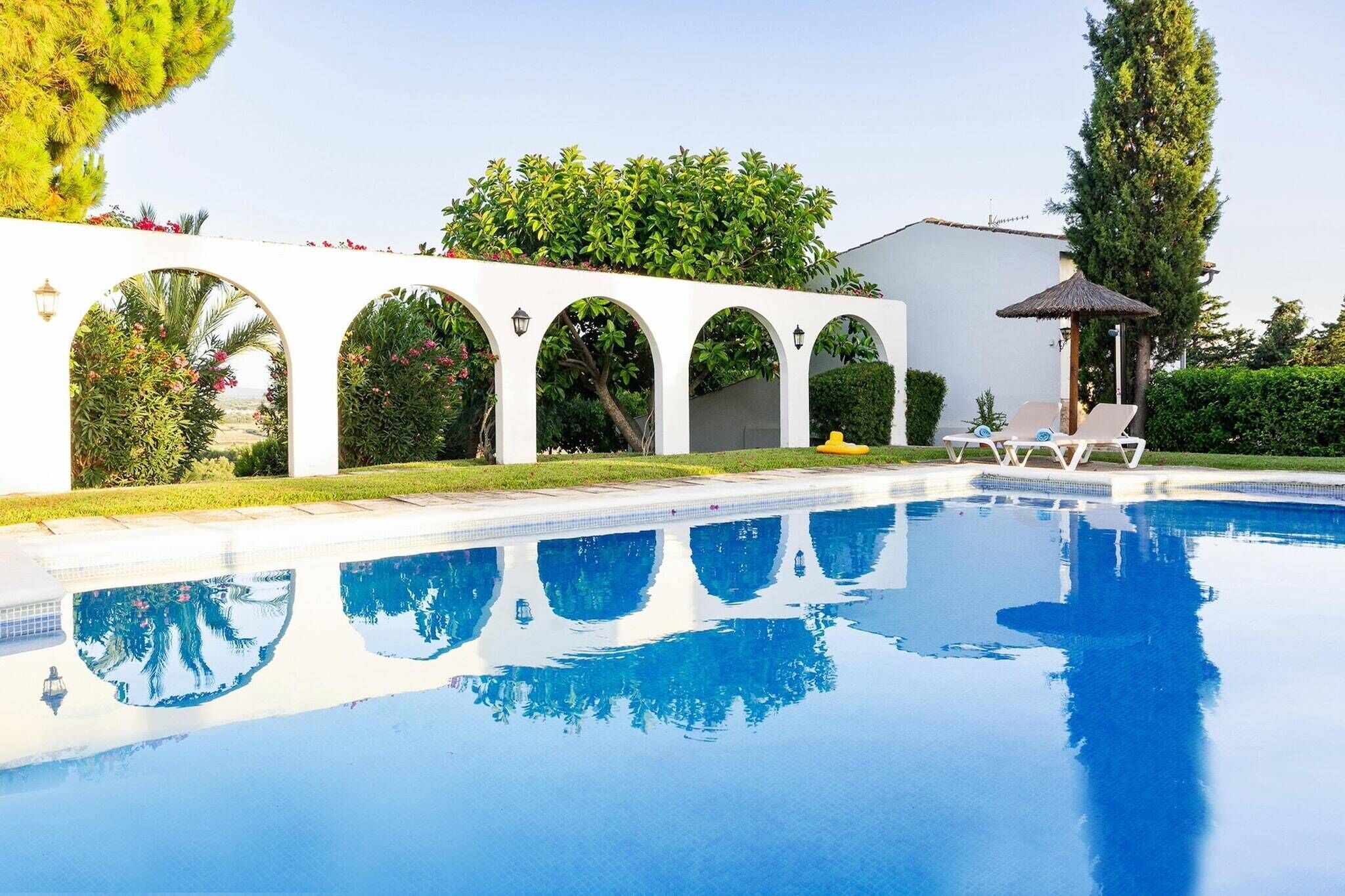 A swimming pool with clear blue water, surrounded by white arches and greenery.