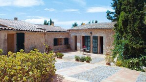 A courtyard with two stone buildings, a paved walkway, and potted plants.