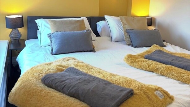 A hotel room with a bed, bedside lamps, a shelf with plants, and a yellow wall. - The Coach House - ultimate home away from home! (Huddersfield)