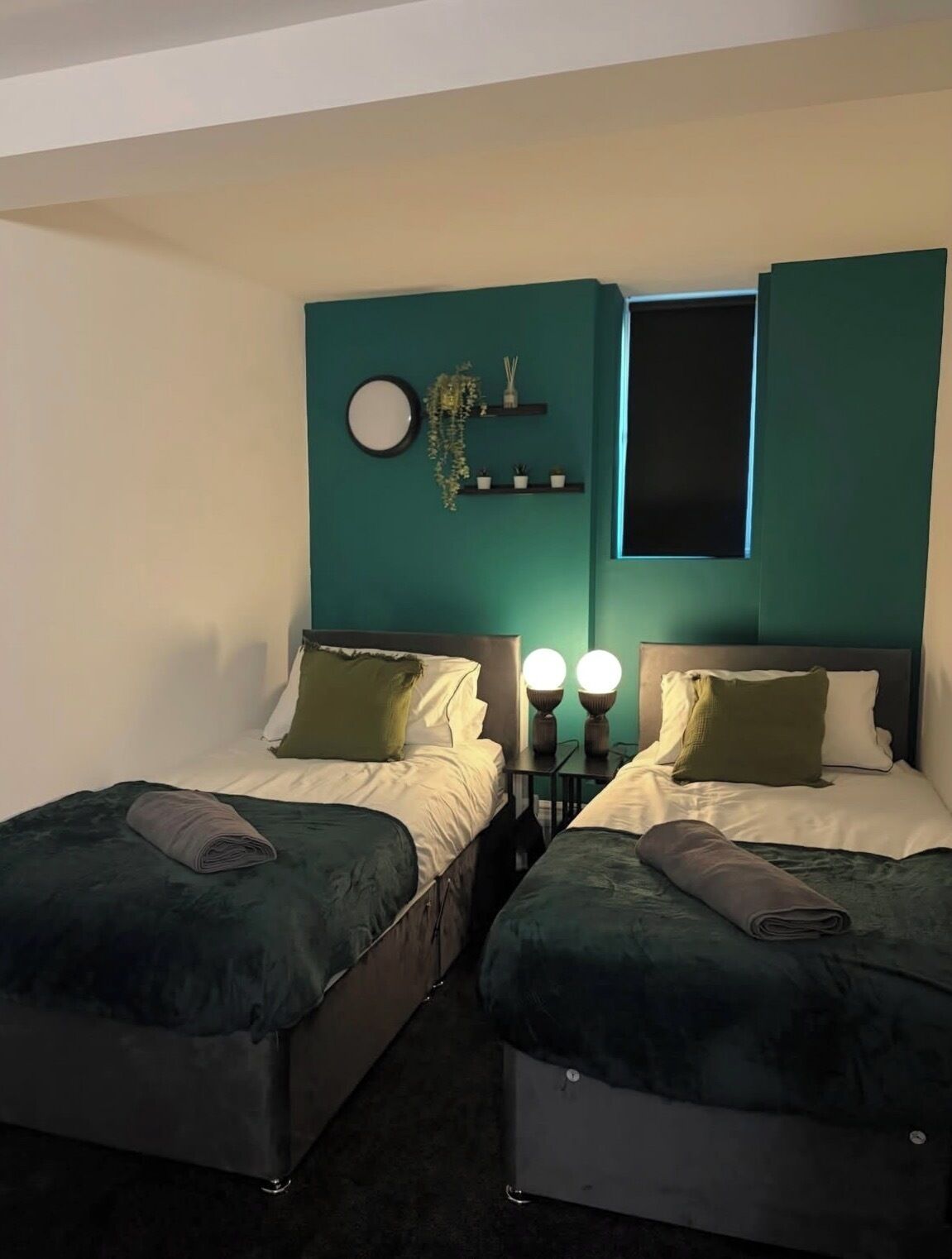 Een tweepersoonskamer met twee bedden, een wandplank met decoratieve objecten, een ronde spiegel en bedlampjes.