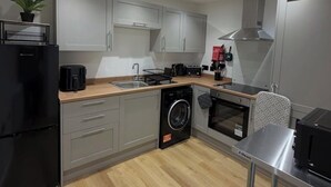 A modern kitchen with grey cabinets, a black refrigerator, a washing machine, a coffee maker, and a microwave. - The Coach House - ultimate home away from home! (Huddersfield)