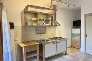 Une cuisine compacte équipée d’une cuisinière intégrée, d’un évier et d’une étagère au-dessus du plan de travail.